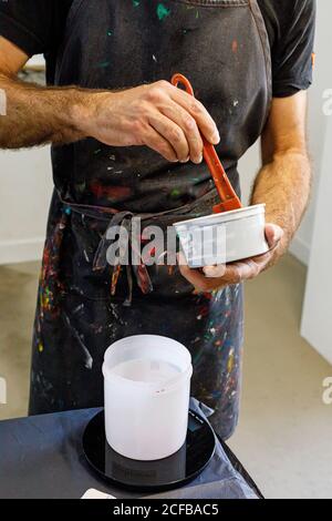 Raccolto concentrato uomo che indossa grembiule sporco che mescola varie vernici per serigrafia in officina Foto Stock