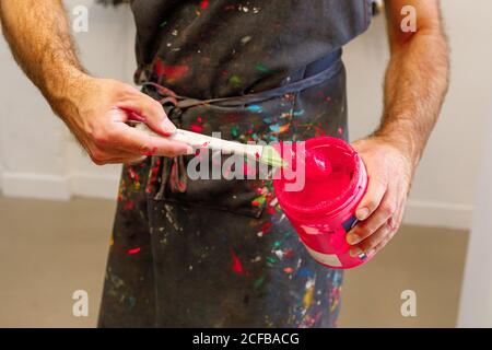 Raccolto concentrato uomo che indossa grembiule sporco che mescola varie vernici per serigrafia in officina Foto Stock