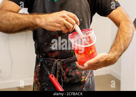 Raccolto concentrato uomo che indossa grembiule sporco che mescola varie vernici per serigrafia in officina Foto Stock