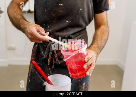 Raccolto concentrato uomo che indossa grembiule sporco che mescola varie vernici per serigrafia in officina Foto Stock