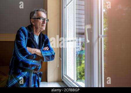 Senior uomo guardando fuori della finestra a casa Foto Stock