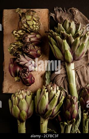 Carciofi freschi mature posti su sfondo nero con tovagliolo e. tavolo di legno Foto Stock