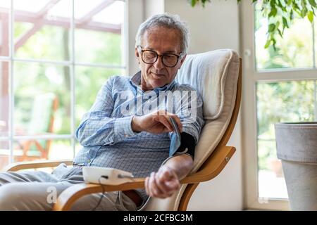 Uomo anziano che usa un dispositivo medico per misurare la pressione sanguigna Foto Stock