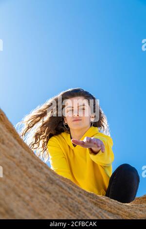 Da sotto brunette Donna in felpa gialla dando mano in rocce di arenaria su sfondo cielo blu Foto Stock