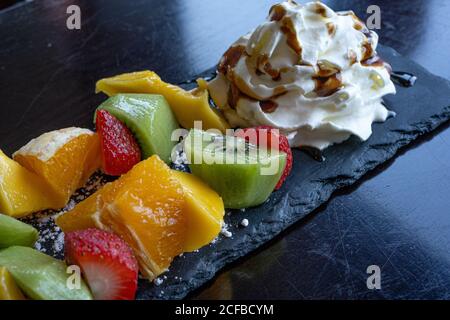 Kebab di frutta fatto di arance, fragole, Kiwi, Mango servito con panna montata. Primo piano della macro. Messa a fuoco selettiva Foto Stock