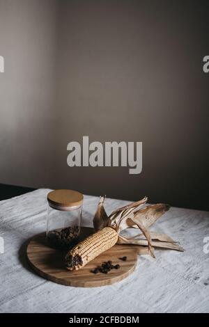 Mais essiccato su pannocchia messo su tavola di legno vicino vaso con spezie marroni sul tavolo da cucina Foto Stock