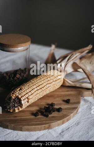 Mais essiccato su pannocchia messo su tavola di legno vicino vaso con spezie marroni sul tavolo da cucina Foto Stock