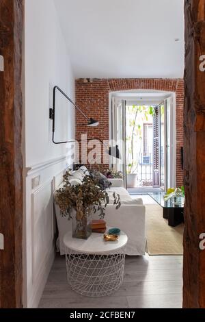 Comodo divano con morbidi cuscini sotto la moderna lampada in metallo vicino a tavoli con decorazioni in elegante e accogliente soggiorno a. casa Foto Stock