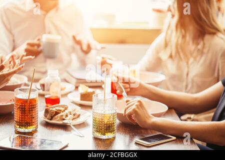 Primo piano foto ritagliata di un tavolo di legno ben servito con gustosi piatti e bicchieri di vino rosso. Il ragazzo sta passando l'insalata fresca all'altro lato della ta Foto Stock