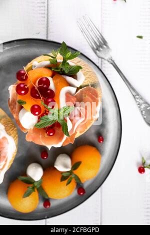 Antipasto italiano con prosciutto di melone e mozzarella decorata con foglie di menta e ribes rosso vista dall'alto colpo di primo piano Foto Stock