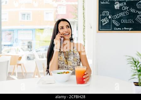 Donna allegra con cibo sano parlando su smartphone in caffetteria Foto Stock