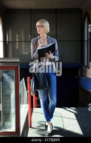 Donna d'affari bionda che cammina con il blocco note Foto Stock