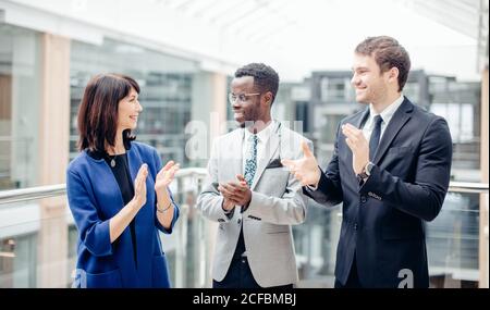 team multinazionale di uomini d'affari che indossano abiti che si aggrappano l'un l'altro o. relatore in un ufficio moderno durante una conferenza o una riunione d'affari Foto Stock