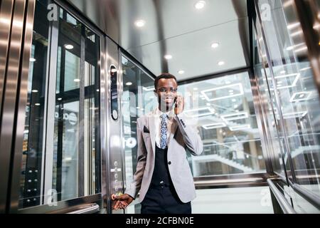 Imprenditore nel moderno ascensore di vetro Parlando dal telefono Foto Stock