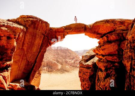 Un uomo beduino si trova sulla cima di un arco di roccia a Wadi Rum, Giordania Foto Stock