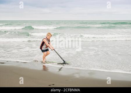Ragazzo giovane che gioca sulla spiaggia con il suo skim board Foto Stock