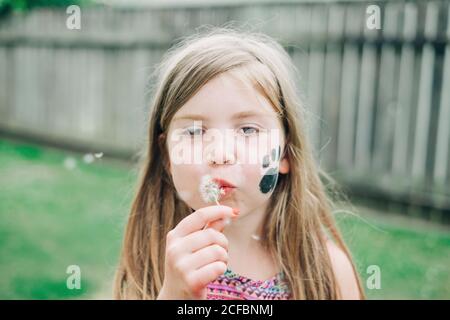 Ragazza giovane che soffia un dente di leone nel cortile Foto Stock