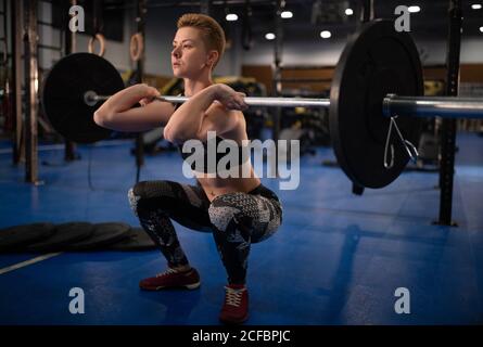 Atleta potente squatting con barbell e fare pulito e a scatti allenati in palestra Foto Stock