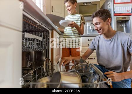 Due ragazzi che caricano la lavastoviglie insieme a casa Foto Stock