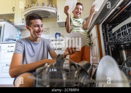 Due ragazzi che caricano la lavastoviglie insieme a casa Foto Stock