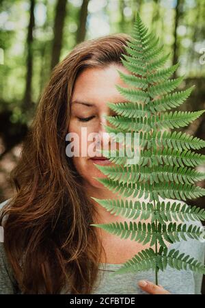 Ritratto di donna con occhi chiusi coprendo il viso con foglia di felce. Foto Stock