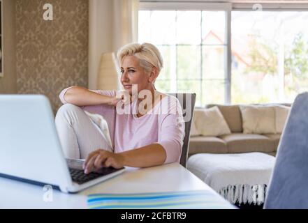 Donna matura utilizzando portatile a casa Foto Stock