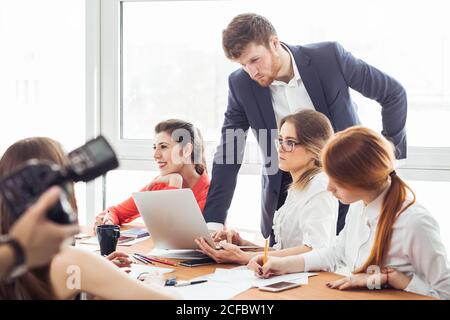 Bel giovane che lavora con il computer e sorride mentre si è in piedi in officina Foto Stock