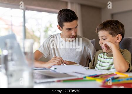 Ragazzo adolescente che aiuta il fratello più giovane a fare i compiti a casa Foto Stock