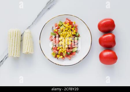 La ciotola è servita con mais, pomodori tagliati e zucchine tavolo con pomodori e mais Foto Stock