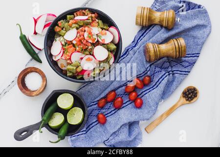Piatto di ciotola con pomodoro tritato e pepe di jalapeno condito con fette di rafano posto su tavola bianca con stagionature Foto Stock