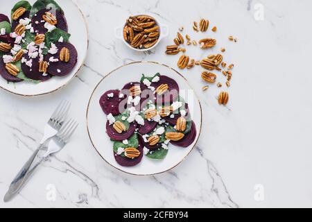 Dall'alto di piatti serviti con fette di barbabietola e. spinaci conditi con un mix di noci pecan e formaggio di capra su tavolo in marmo Foto Stock