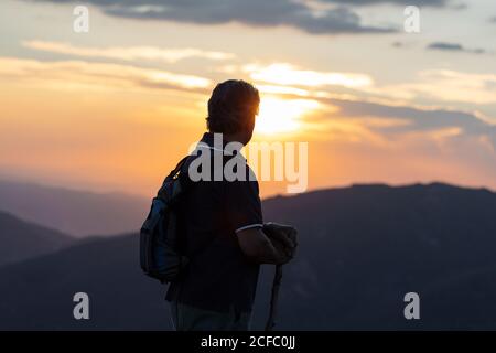 Silhouette di vista posteriore di un uomo anziano con la schiena pack e bastone di legno escursione contemplando paesaggio di montagna incredibile Foto Stock