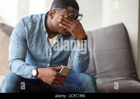 Sensazione di sfinito. Frustrato giovane uomo nero massaggiando il naso e mantenendo gli occhi chiusi mentre si siede al suo posto di lavoro in ufficio Foto Stock