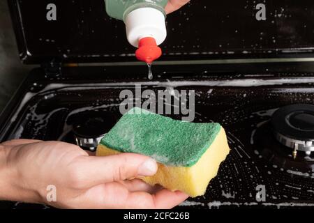 la ragazza applica il detergente ad un primo piano di washcloth giallo, pulendo la superficie sulla stufa a gas. Foto Stock