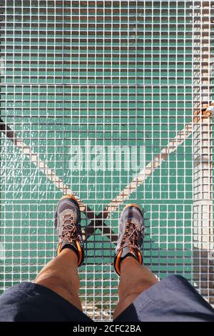 Vista dall'alto delle gambe dell'uomo irriconoscibili che si erigano su un ponte di montagna sopra un fiume. Foto Stock