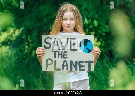 Attivista bambina con salvare il manifesto del pianeta nel parco forestale. Presteen capretto volontario lotta contro l'inquinamento, riscaldamento globale, riciclare i rifiuti. Ecolog Foto Stock