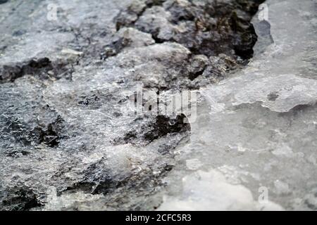 Sciogliendo ghiaccio e neve sulla superficie rocciosa con ciottoli alla luce del giorno Foto Stock