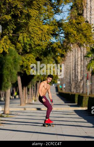 Giovane ispanico a corpo pieno con zaino in skateboard marciapiede durante il giorno di sole sulla strada della città Foto Stock