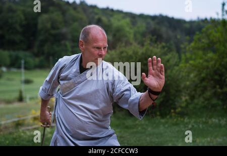 Determinato maschio di mezza età in kimono focalizzare e usando la spada mentre si allenano da soli in giardino Foto Stock