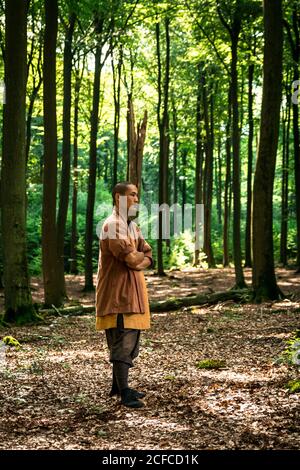 Ragazzo asiatico in marrone uniforme gesticulating mentre fa arti marziali esercizio fisico durante l'allenamento nella foresta verde Foto Stock