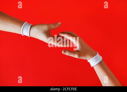 Dia una mano d'aiuto. Mani con braccialetti bianchi che si avvicinano l'uno all'altro sullo sfondo rosso. Foto Stock