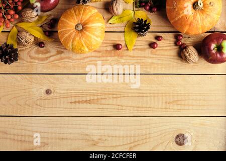 Buon giorno del Ringraziamento. Cornice autunnale fatta di zucche d'arancia mature, foglie cadute, frutta, noci su tavola rustica di legno. Disposizione piatta, vista da abo Foto Stock