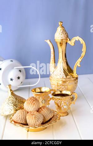 Concetto Ramadan. Maamoul tradizionale arabo farcito pasticceria o biscotti con datteri o noci serviti con caffè dorato set. Dolci orientali. Primo piano. Bianco WO Foto Stock