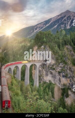 Treno su ferrovia su ponte ad arco da tunnel in verde foresta in Svizzera Foto Stock