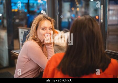 Giovani donne multirazziali sorridenti e che parlano tra loro sedersi al tavolo in un'accogliente caffetteria divertendosi Foto Stock