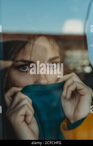 Pendente giovane donna triste con i dreadlock appoggiati al vetro della finestra e guardando via Foto Stock