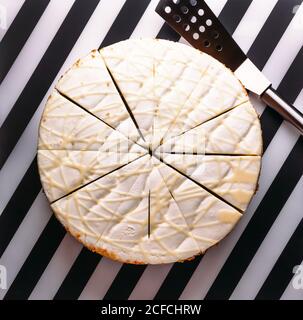 Vista dall'alto della torta rotonda con panna bianca e smalto tagliate a pezzetti per servire su bianco e nero superficie striata Foto Stock