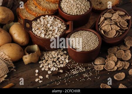 Da sopra cereali semi di farinata d'avena in ciotole patate e affettati pane su sfondo di legno Foto Stock