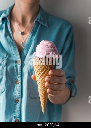Gelato a mano nel cono. Paletta gelato in cono in mano Donna. Verticale Foto Stock