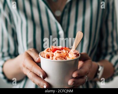 Gelato arrotolato con fragola in tazza conica in mani di Donna. Tazza conica con gelato arrotolato in stile tailandese Foto Stock